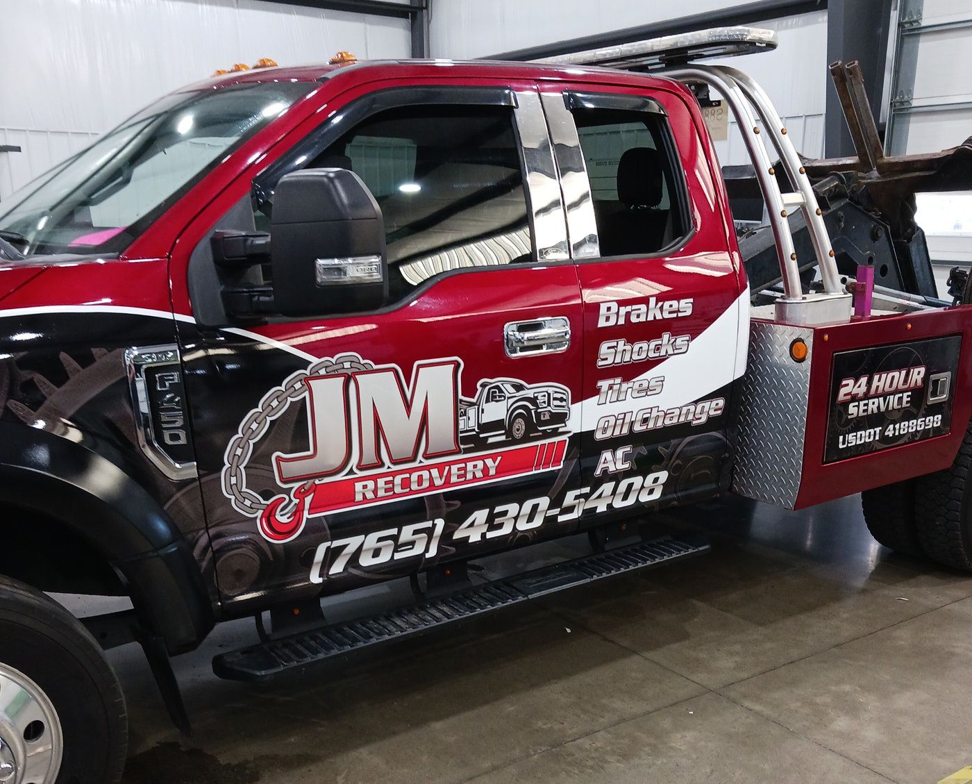 Red tow and recovery truck with black and white graphics and phone number
